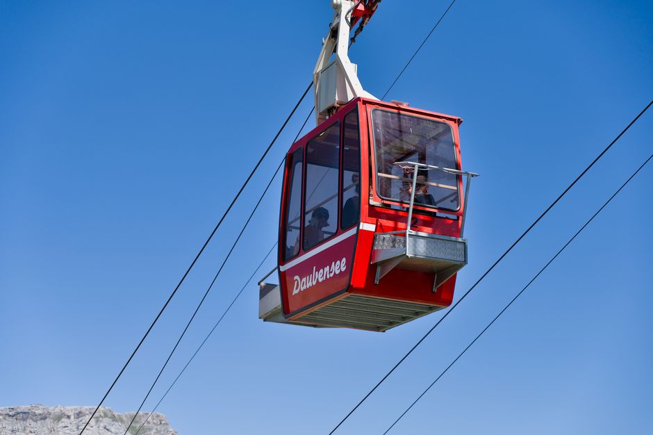 Red cable car traveling over Daubensee in Swiss Alps with clear blue sky.
