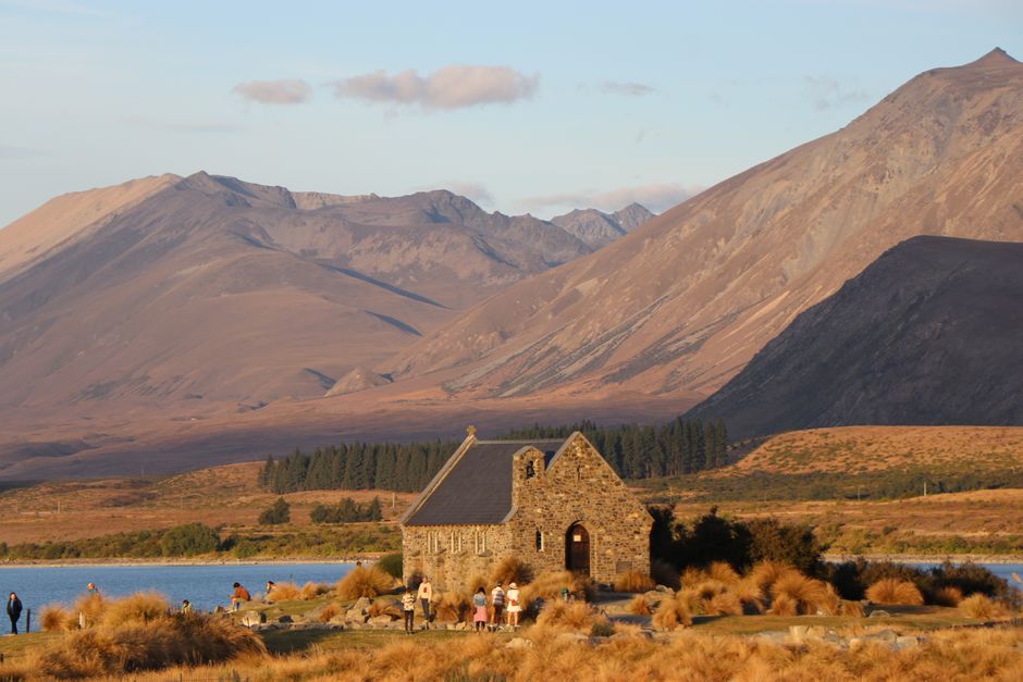 Beautiful chapel near lake with mountain backdrop under clear sky. Scenic view with people enjoying the outdoors.