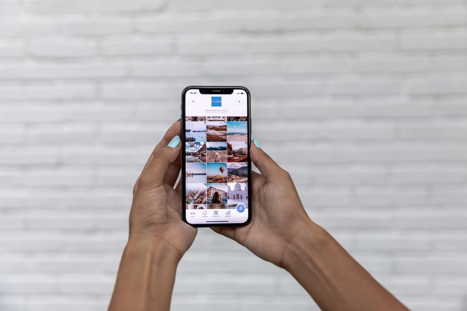 Close-up of woman holding a smartphone displaying a social media app against a brick wall.
