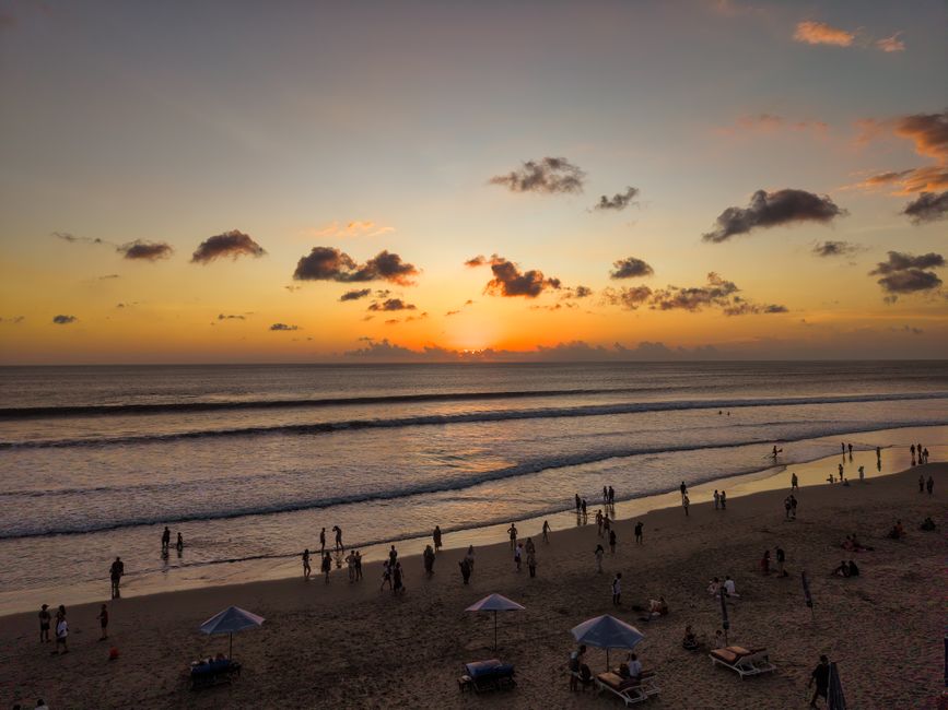 Stunning Bali sunset at Kuta Beach with silhouettes of people on the shoreline.