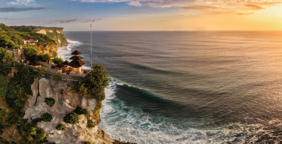 A breathtaking aerial view of Uluwatu Temple perched on cliffs overlooking the ocean at sunset in Bali, Indonesia.