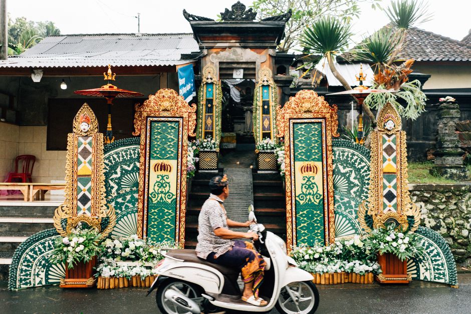 A Balinese person rides a scooter past ornately decorated temple gates, showcasing cultural traditions.