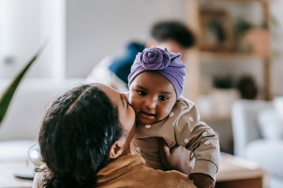 Tender African American mother kissing cute little African American daughter while caressing in living room on blurred background at home