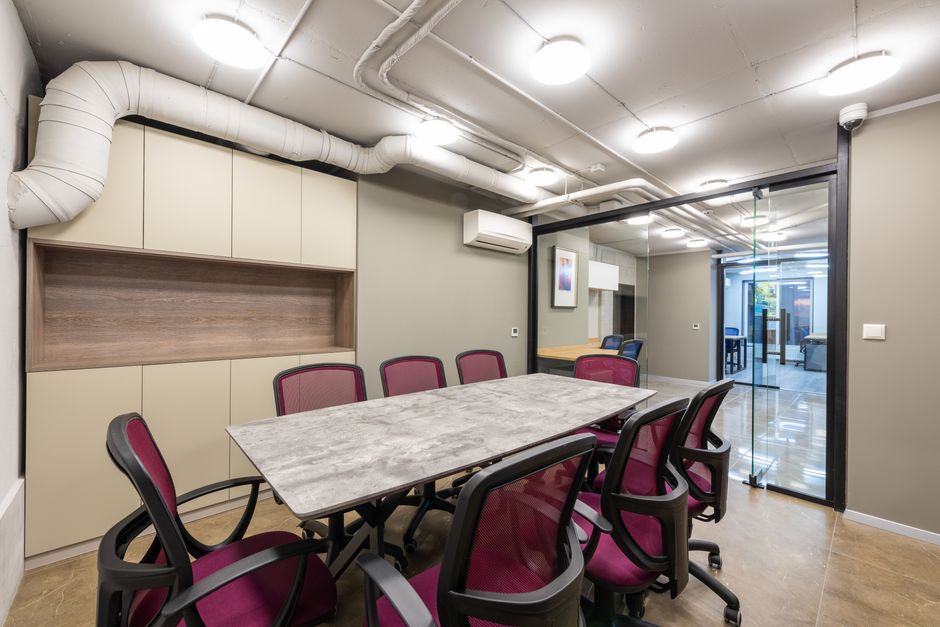 Modern conference room with table and office chairs under ceiling with glowing lamps located behind glass doors