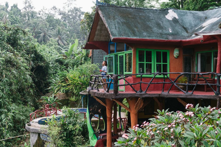 Unrecognizable female traveler chilling on terrace of cozy colorful house surrounded by green tropical jungle