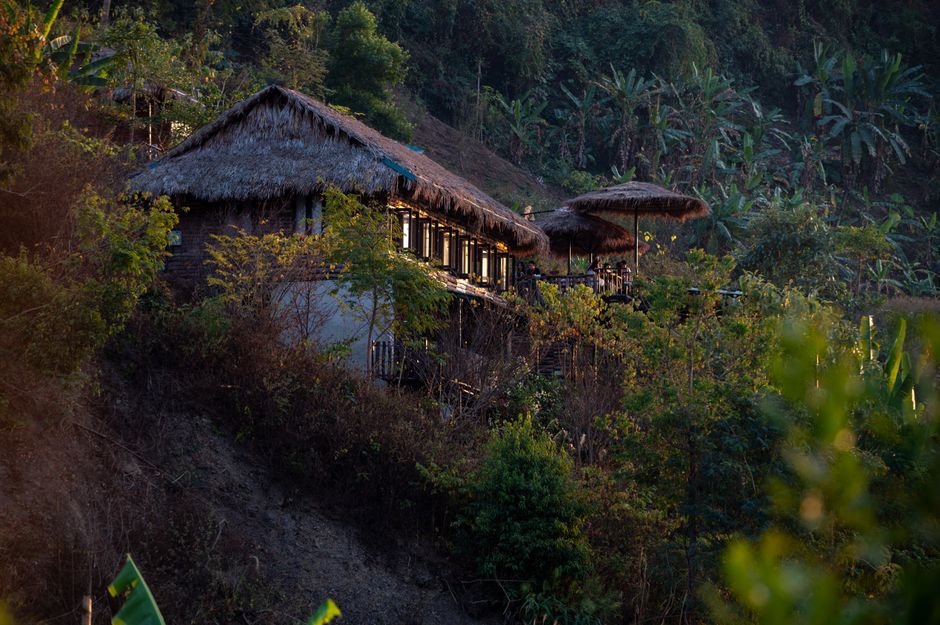 A traditional hut with a thatched roof nestled on a lush hillside overlooking dense jungle foliage.