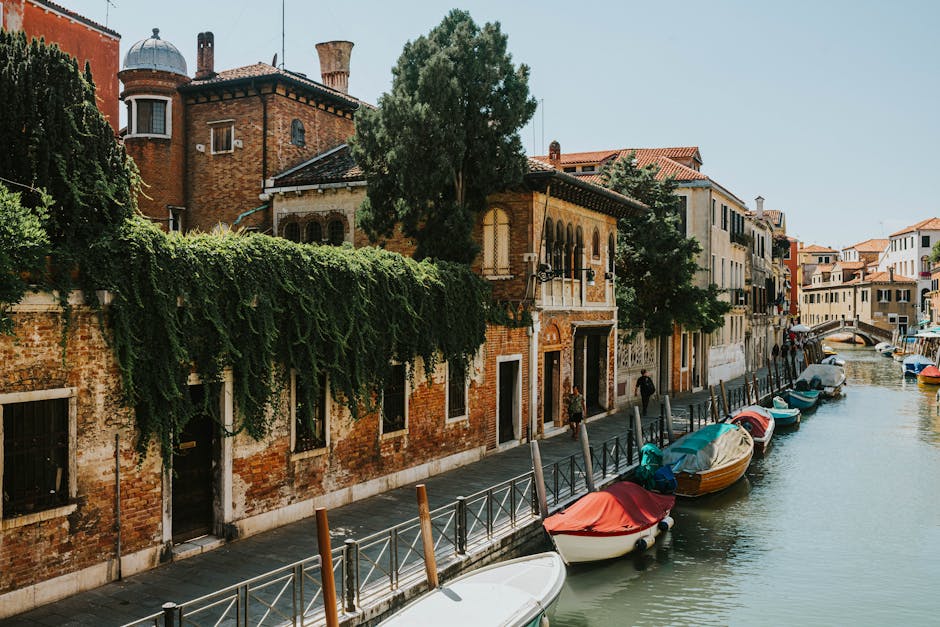 Charming canal in Venice lined with historic buildings and moored boats under a clear sky.