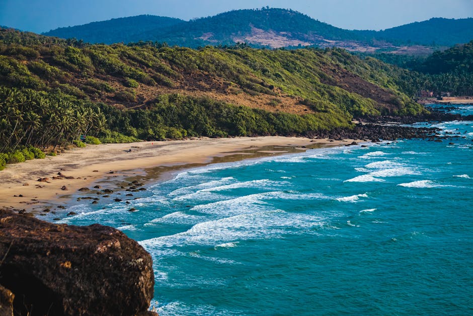 Breathtaking view of a serene beach with crashing waves and lush green hills.