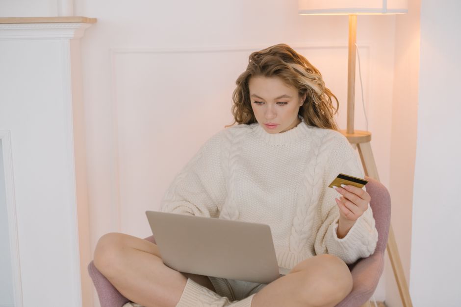 Young woman in a cozy sweater shopping online using a laptop and credit card.