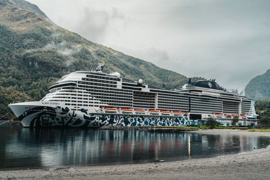 Cruise ship docked in a scenic Norwegian fjord surrounded by mountains.