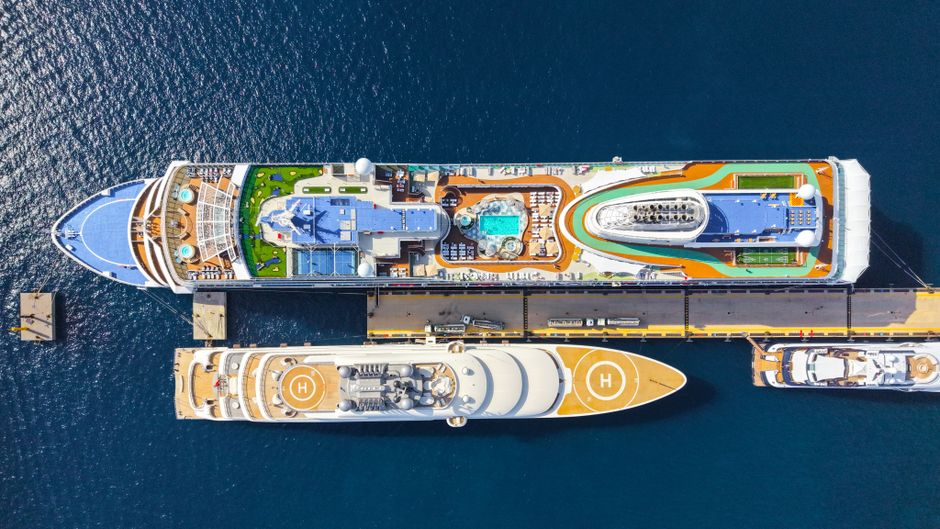 Top-down view of two luxurious cruise ships moored at a sunny port, showcasing pools and helipads.