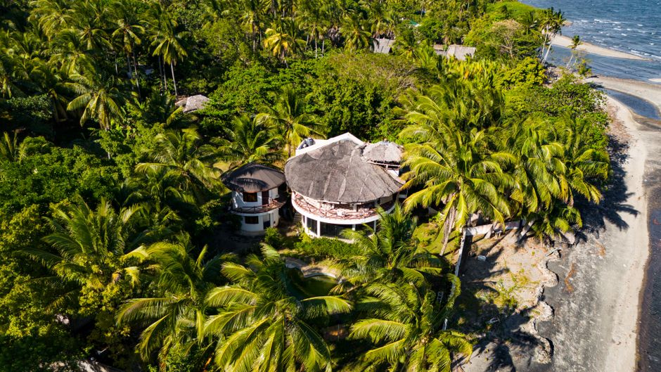 Aerial view of a tropical beach house surrounded by lush palm trees in Bacong, Philippines.