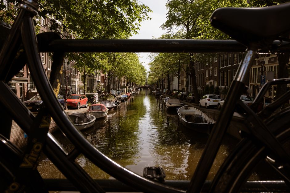 Beautiful view of an Amsterdam canal framed by a bicycle, showcasing classic Dutch architecture.