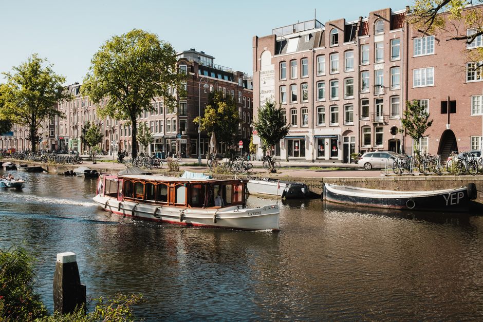 A boat travels down an Amsterdam canal lined with historic buildings and bicycles.