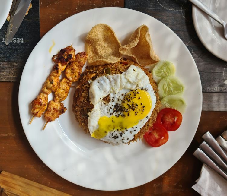 Top view of Nasi Goreng served with fried egg, satay, and fresh vegetables.