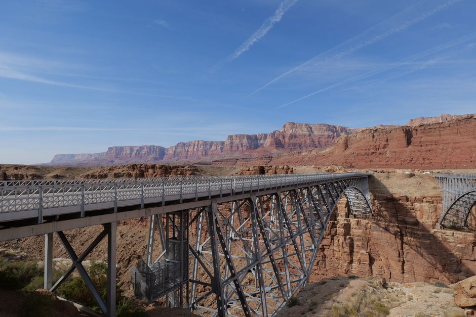 Scenic view of Navajo Bridge over Colorado River with Arizona's red cliffs under a clear blue sky.