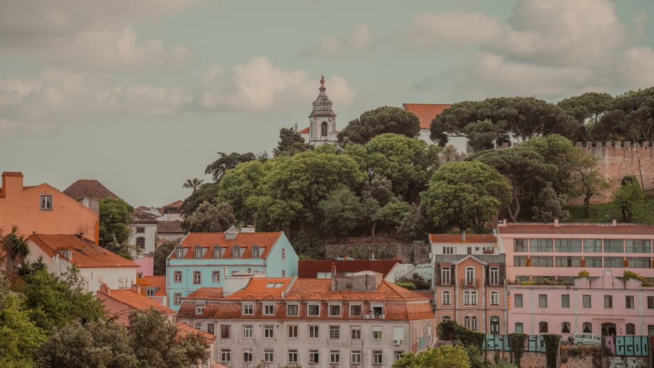 Picturesque view of Lisbon's colorful buildings and lush trees under a cloudy sky.