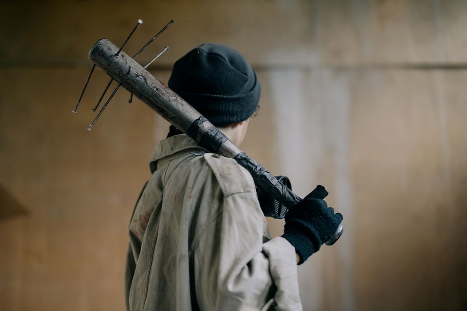 Person in rugged setting with a makeshift weapon, back view.