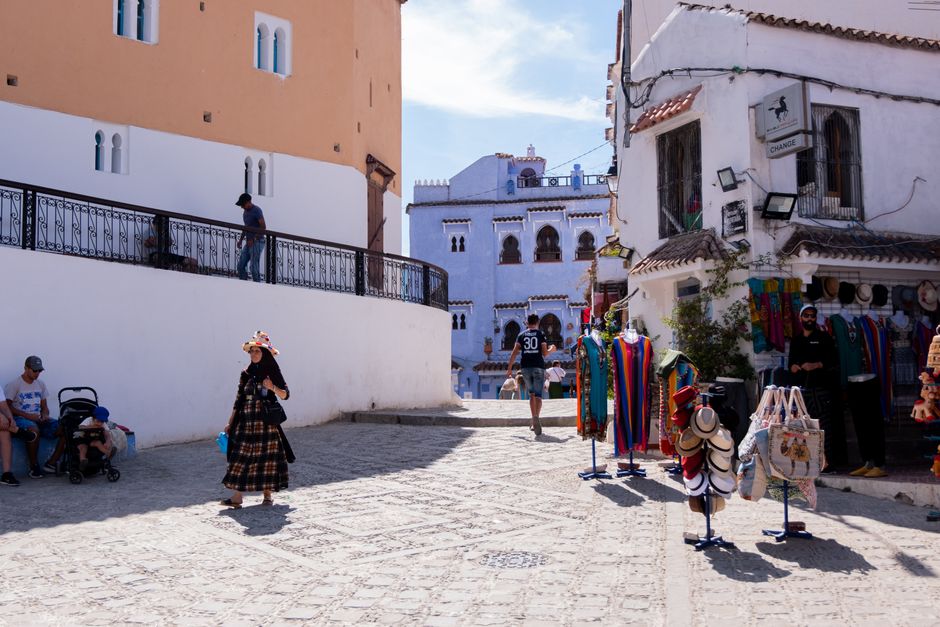 A vibrant street in Chefchaouen with local shops and people enjoying the sunny day.