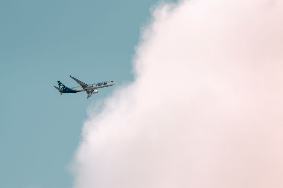 Alaska Airlines plane soaring through a bright sky with fluffy clouds in Seattle.