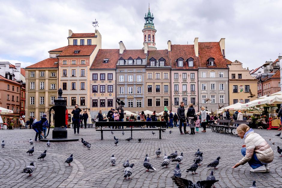 Charming Old Town Square in Warsaw bustling with people, pigeons, and elegant historic buildings.
