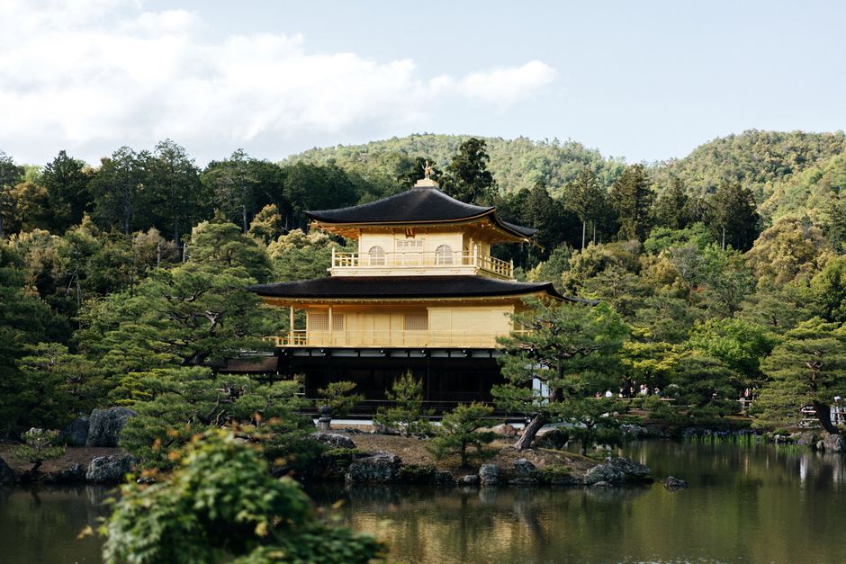 Beautiful view of the Golden Pavilion, Kinkaku-ji Temple, reflected in a serene pond in Kyoto's lush green setting.