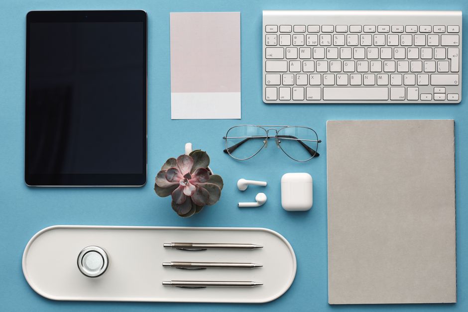 Top view of a minimalist workspace with tech gadgets and office accessories on a blue background.