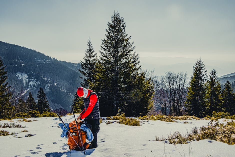 A hiker prepares gear amidst snowy mountains and winter trees, capturing the adventure spirit.