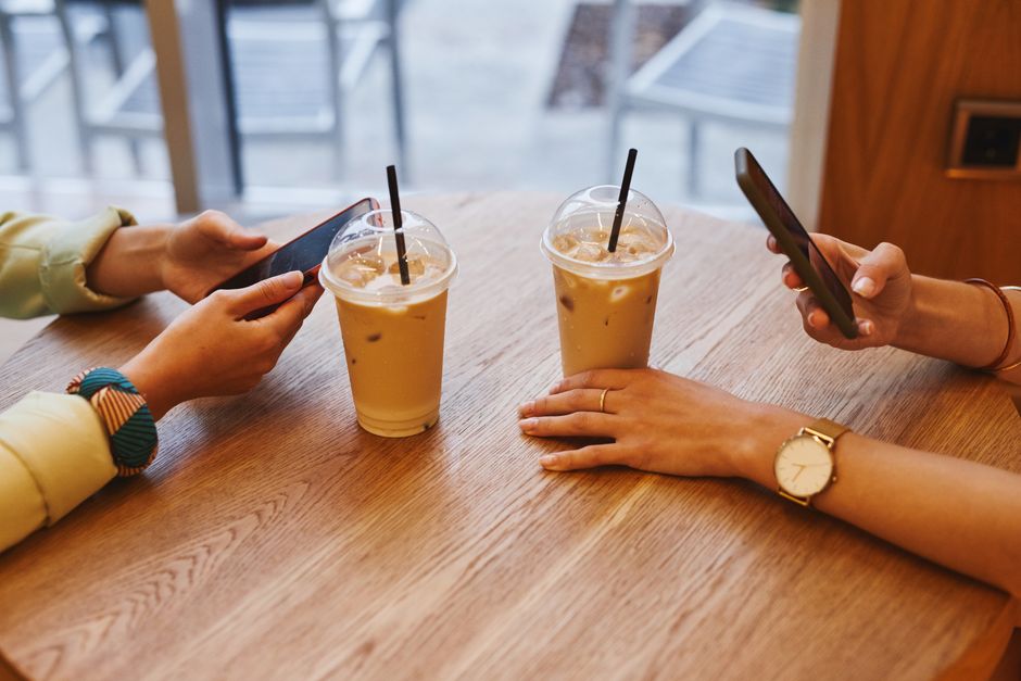 Two people enjoying iced coffee and using smartphones in a cozy cafe setting.