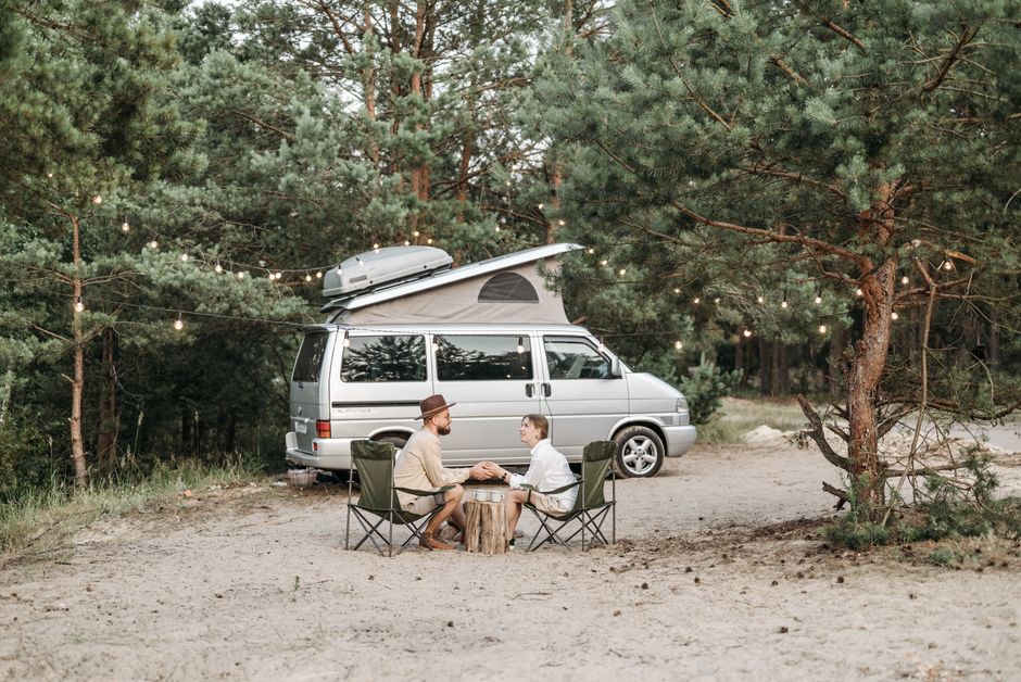 A couple sitting by a camper van in the forest, enjoying a tranquil outdoor camping experience.