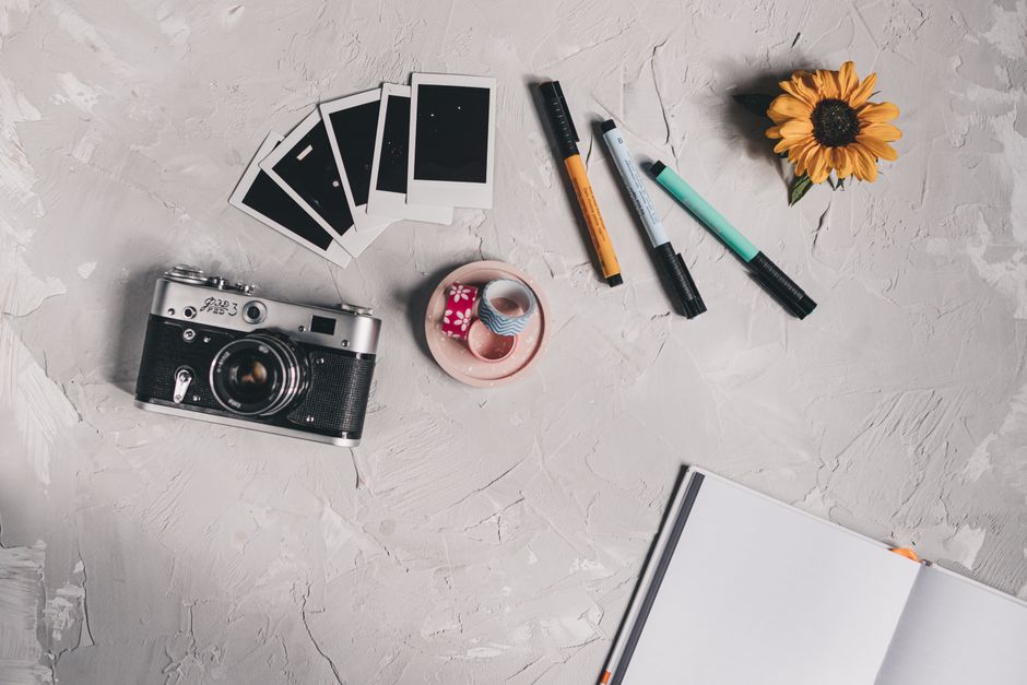 Flat lay of a creative workspace featuring a vintage camera, notebooks, and colorful pens.