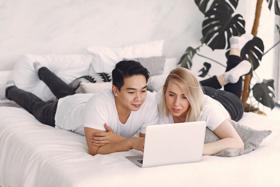 Young couple enjoying leisure time together streaming videos on a laptop in a cozy, modern bedroom.