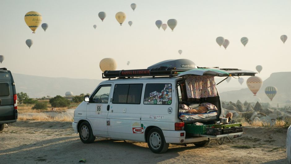 Explore the scenic views of Cappadocia with hot air balloons flying over a camper van at sunrise.