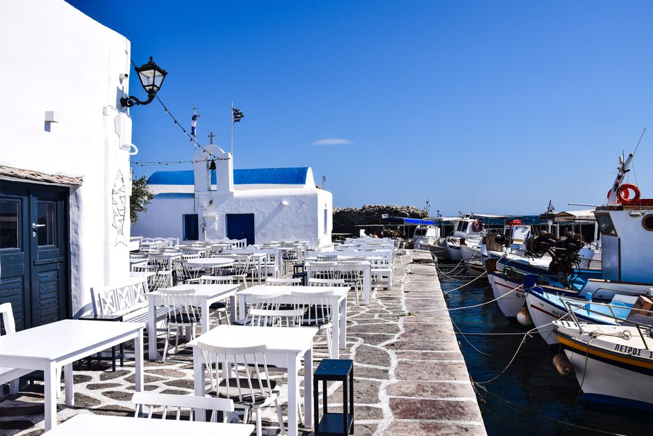 Scenic view of a Greek seaside restaurant with motorboats moored at the marina, perfect for a summer vacation.