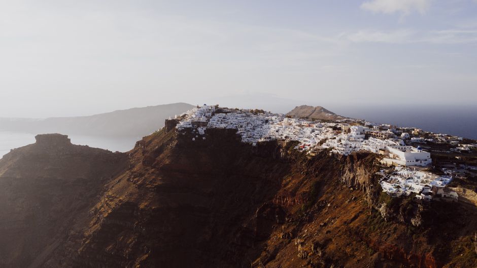 Stunning aerial view of Fira, Santorini with iconic white buildings on a cliffside under a clear sky.