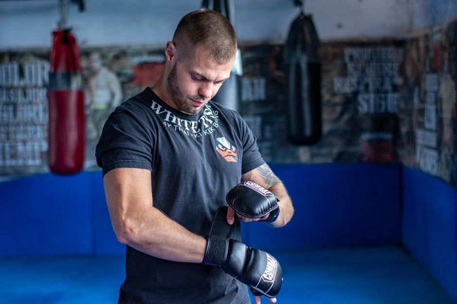 Muscular man adjusting boxing gloves in a gym, embodying strength and focus in sportswear.