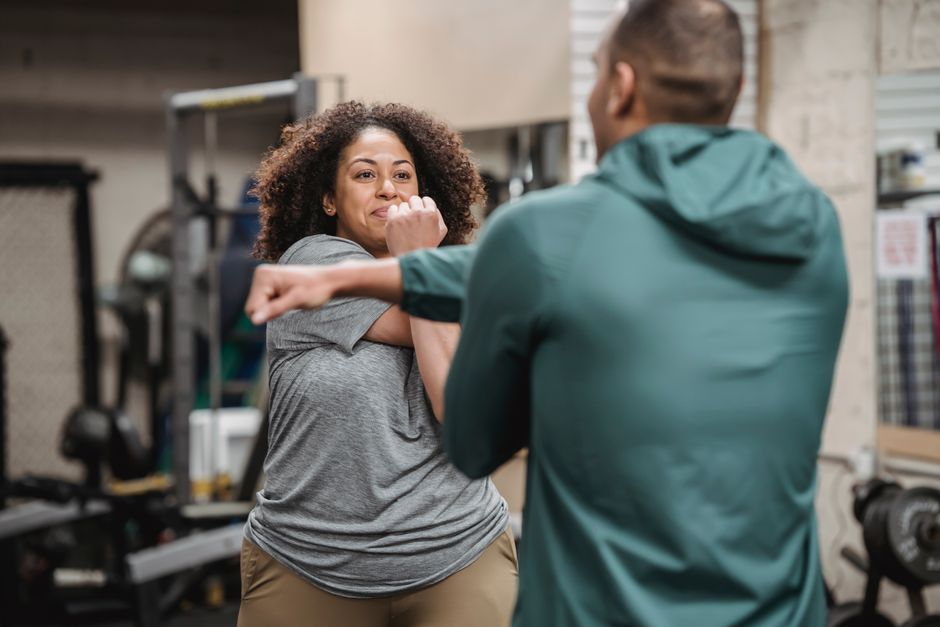 Crop anonymous instructor training overweight happy African American female in gym with workout equipment
