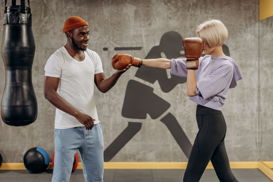 A female athlete spars with her coach in a gym, practicing boxing techniques indoors.
