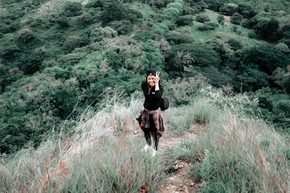 A woman enjoying a hike in a lush green mountain area, smiling at the camera.