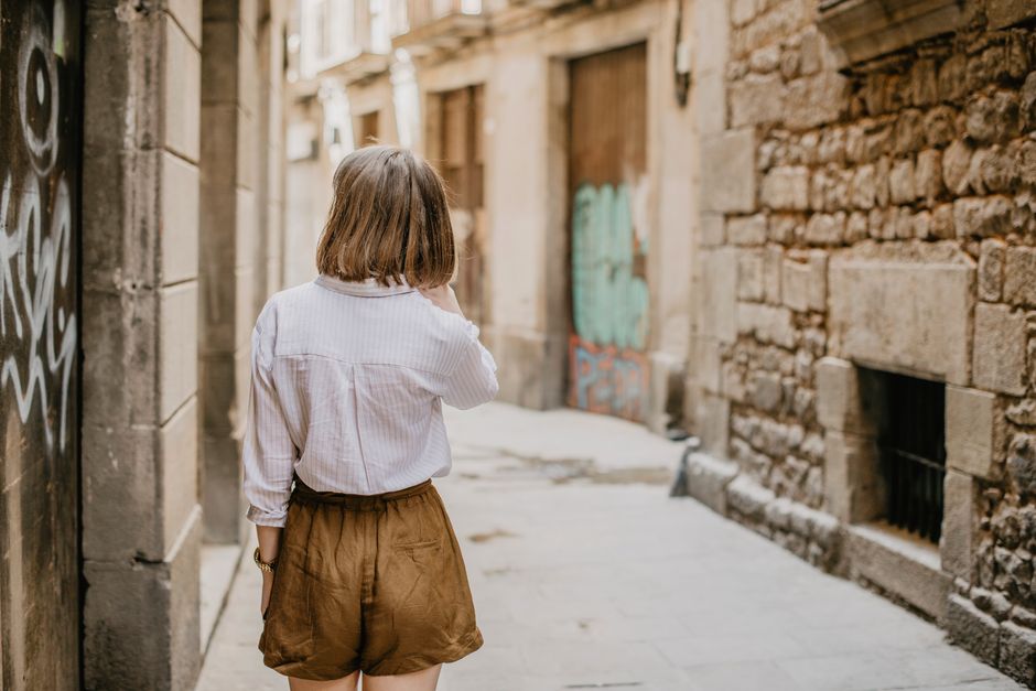 Woman in casual attire walks through a rustic urban alleyway during summer.