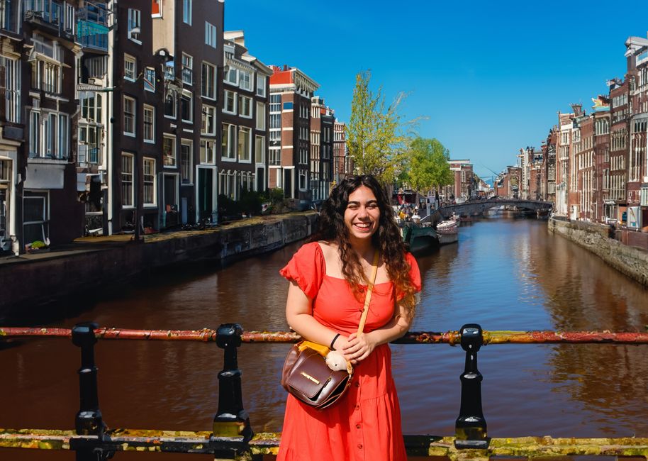 A cheerful woman in a red dress on a bridge over Amsterdam's picturesque canals on a sunny summer day.