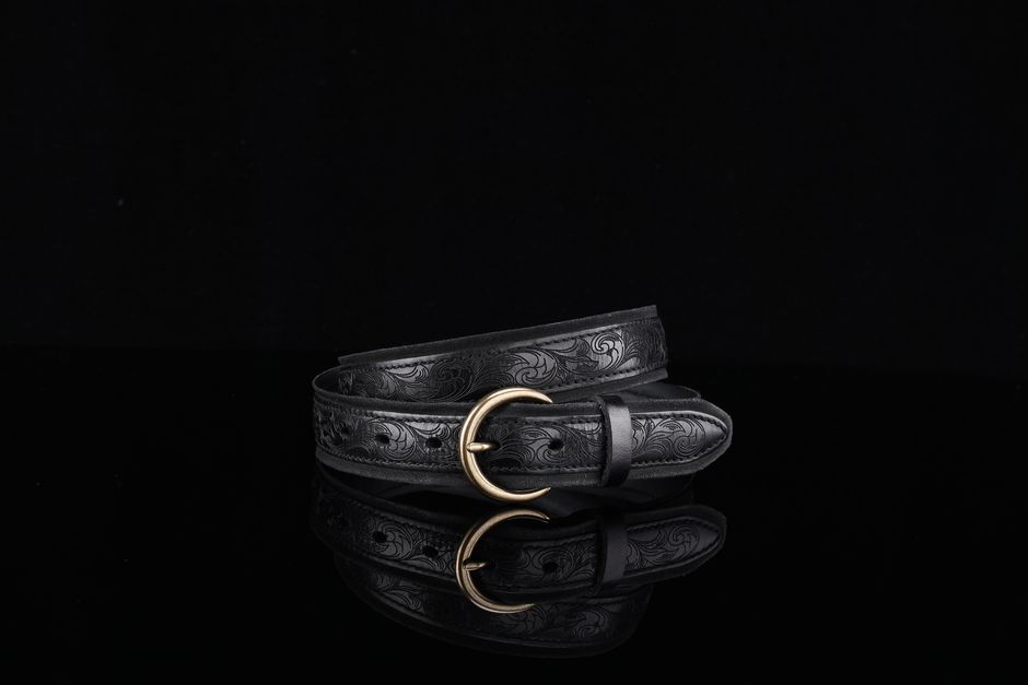 Stylish black leather belt with intricate embossing and brass buckle on black background.