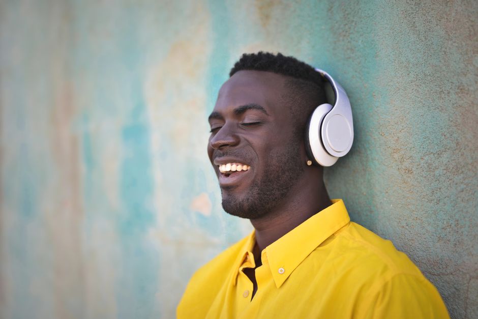 Happy young man enjoying music with headphones against a textured wall outdoors.
