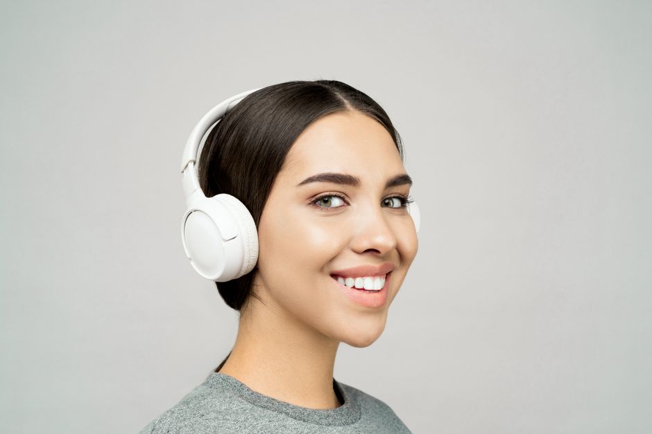 Cheerful young woman wearing headphones and smiling indoors, enjoying music.