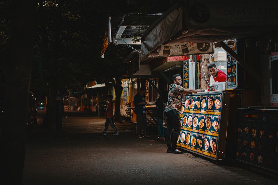 A vibrant night scene capturing an interaction at a street food stall with illuminated menus.