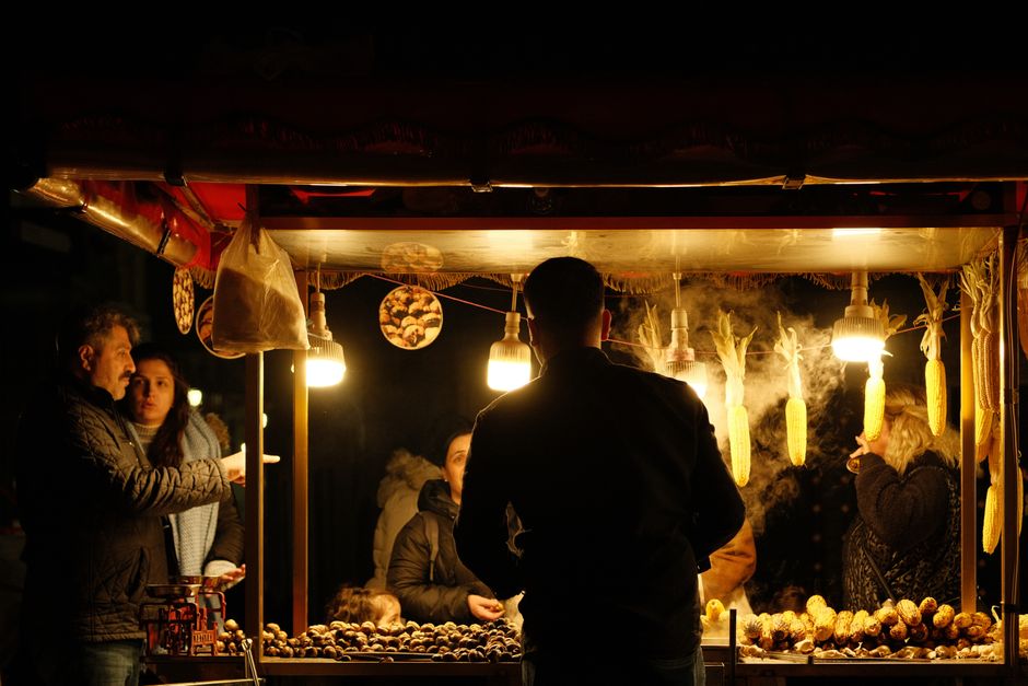 Street food stand at night with people enjoying roasted corn.