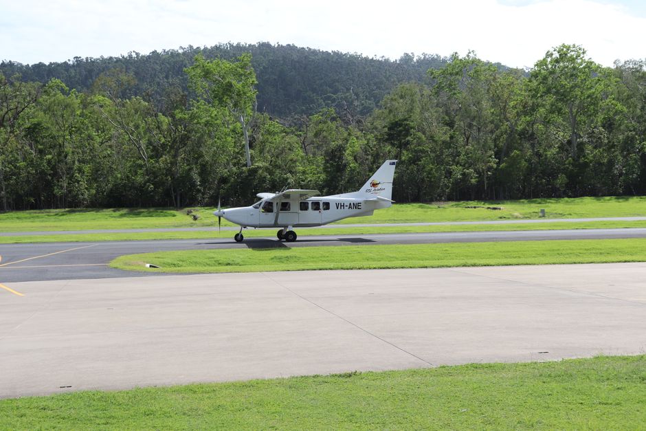 Small aircraft taxiing on a runway surrounded by lush greenery and forest backdrop.
