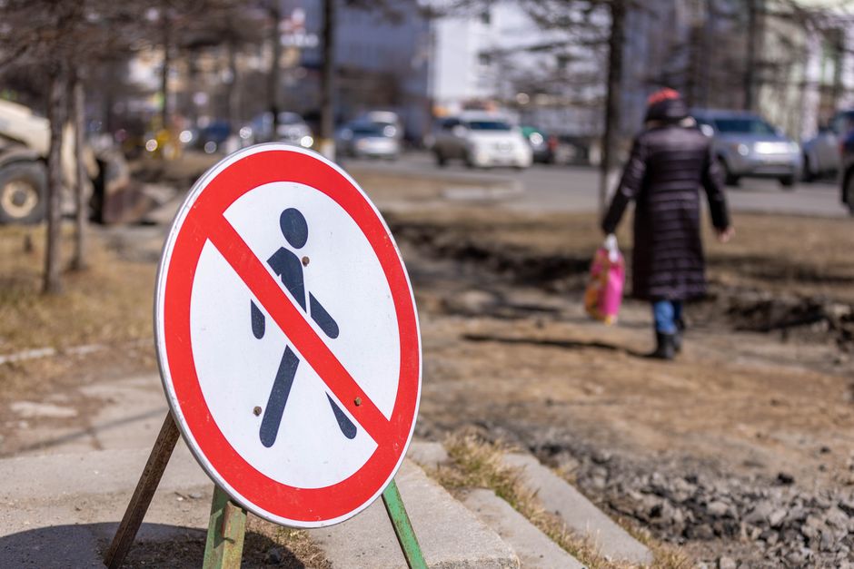 Close-up of a no pedestrian sign on a city street with blurred background traffic, highlighting urban safety.