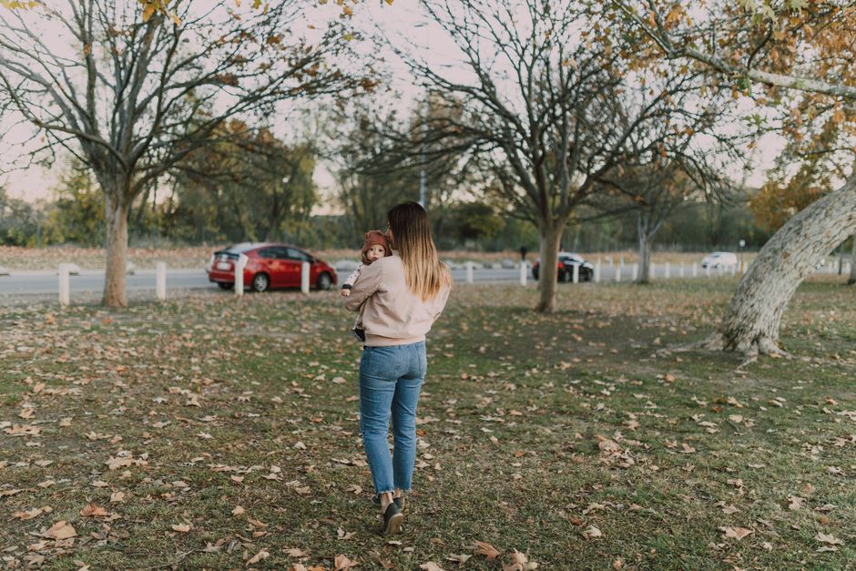 A woman carrying her baby through a serene autumn park. Captured on a sunny day.